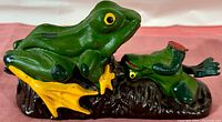 Side view of the painted cast iron mechanical coin bank depicting a green frog and a smaller frog on a textured base.