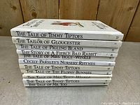 Side view stack of 11 hardcover Beatrix Potter books printed in 1986 featuring titles on spine such as The Tale of Timmy Tiptoes, The Tailor of Gloucester, and others.