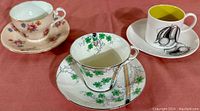 Three vintage bone china cups and saucers on a red cloth, showing various floral and botanical designs