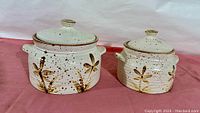 Two vintage Laurentian Pottery covered casseroles side by side on a pink surface, showing full design and lids in place.