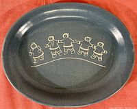 Top down view of oval stoneware platter showing Inuit figures etched in blue glazed surface.