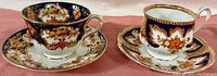 Two Royal Albert Crown China Imari pattern tea cups and saucers displayed on a cloth, showing intricate gold and cobalt blue designs.