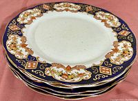 Photo showing 5 stacked Royal Albert dinner plates with decorative cobalt blue and gold borders and floral accents.
