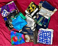 Overview of the collection of folded vintage silk scarves in varied colors and patterns arranged on a red surface.