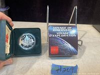 Obverse side of the 2000 Canadian proof silver dollar coin showing the space shuttle design and display case with certificate booklet titled 'Voyage of Discovery'.