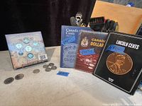 Photo showing 2004 Oh! Canada Gift Set with coins displayed on coin specification card, Canada Cents book, Canada Dollar book with empty holder, Lincoln Cents book with few pennies, and some loose coins including U.S. pennies on table.
