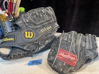 Three vintage baseball gloves stacked showing Wilson branding in gold and Rawlings red logo patch.