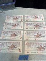 Eight uncirculated 1986 $2 bills arranged on a table showing front sides with bird illustrations and sequential serial numbers.