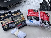 Display of various new socks including black and gray Workload cushioned socks, Mountain Ridge thermal socks, and white crew socks in plastic packaging.