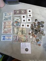 Wide view of the lot showing foreign paper bills, coins in protective holders, loose coins, and the Washington medallion with information card.