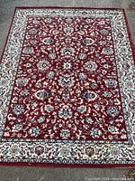 Top-down photo of a rectangular machine made rug with a red base and cream floral border, showing the entire rug laid flat.