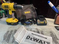 Yellow and black DEWALT 18V cordless drill with attached battery, battery charger, spare battery, and carrying case with instruction manual on table.