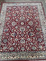 Full view of the machine made area rug showing the red floral field and cream floral border.