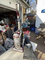 Full view of upright Shark vacuum cleaner showing handle, dust canister, and brush head with hose attachment coiled beside it.