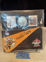 Front view of collectible set featuring two Canadian stamps and a 25 cent coin in protective packaging with Hamilton Tiger-Cats and Grey Cup graphics.