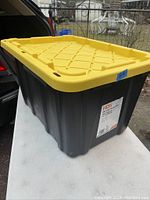 Photo showing the black storage tote with yellow lid from an angle, highlighting lid design and overall size.
