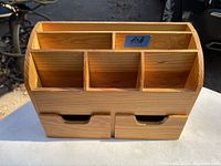 Front view of the wooden organizer showing the six compartments and two drawers with a blue sticker.
