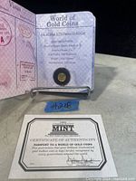 Close-up photo of the Isle of Man 1/25 ounce gold cat coin in its display holder that resembles a passport, showing detailed text with specifications including gold purity, weight, and designs.