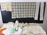 Photo showing multiple lace pieces including a large geometric crocheted table runner, smaller lace trims, and doilies in cream tones against a black background.