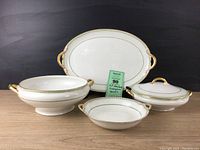 Full view of four serving pieces: platter, two covered dishes and serving bowl, showing pattern and gold trim.