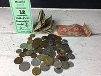 Photo showing folded vintage banknotes and a large pile of assorted international coins on a white surface.