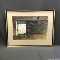 Framed watercolor artwork 'Door In The Wall' depicting a white wooden door in a textured old wall environment with ground in front, all in muted natural tones.