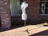 Front view of the gray fabric-covered dress form mounted on a metal tripod stand, showing its full 54 inch height and sturdy base.