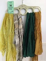 Four scarves hanging on beige plastic four-ring scarf hanger, including a yellow scarf and three scarves from Eileen Fisher