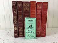 Photo showing six Franklin Library classics standing side by side with a Maxsold tag for identification.