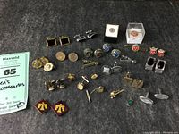 Full collection of men's accessories including cufflinks, tie clips, tie pins, and coins laid out on dark fabric.