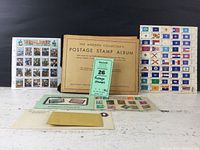 Photo showing the full view of the antique Modern Collector's Postage Stamp Album, two full sheets of stamps (Civil War and State Flags), and two small envelopes with additional stamps.