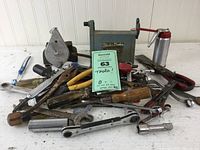 Photo showing a pile of hand tools including a Black & Decker chalk line, metal oil can with red nozzle, and assorted screwdrivers and wrenches in used condition.