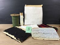 Full overview of vintage lace and ribbon yardages including box of white lace, black lace trim, blue lace with sequins, green ribbon spool, white lace spool, multicolored woven ribbons.