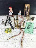 Lot of watches, dolls, pens, lighter, pin, and braided cord on white surface against black background