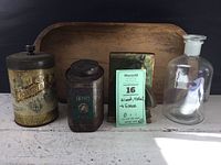 Overview of all items in the collection: two tins, wooden trencher, glass bottle with stopper, and brass bookend