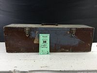 Closed rectangular wooden tool box showing mostly natural wood front with worn blue paint patch, two metal latches, and handle on top.