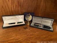 Two ballpoint pen sets displayed with a small globe paperweight on wood background.