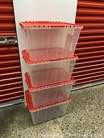 Four of the clear plastic storage bins stacked with red lids on top, showing size and shape.