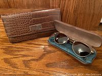 Buffalo leather wallet and sunglasses in a blue velvet-lined case, wallet closed showing crocodile pattern and metal logo plate