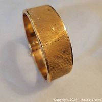 Angled view of bangle showing embossed starburst design and hinge.