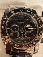 Close-up of the watch face showing black dial, silver-tone markers, three subdials and tachymeter bezel.