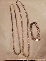 Full view of two necklaces and one bracelet laid out flat on a cloth surface showing different chain styles and clasp on bracelet.