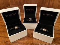 Three silver Pandora charms in separate white display boxes on a wooden surface.