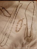 Overview of various silver toned necklaces and a bracelet on a beige surface.