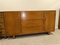 Front angle showing full wooden buffet with three central dovetailed drawers and two side doors, on carpeted floor against wall.