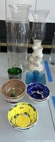 Photo of glass vases, candleholders, small bowls, and decorative glass pieces arranged on a flat surface.