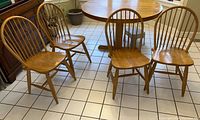 Set of four wooden dining chairs in light honey finish with spindle backs and contoured seats shown on tiled floor near wooden table.