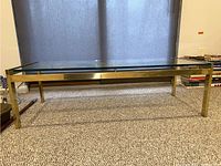 Full view of the rectangular coffee table showing the glass top and brass frame on carpeted floor with closed curtains in background.