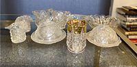 Collection of cut glass candy dishes with lids, two candle holders and three pressed glass creamers on glass shelf.