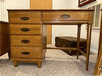 Front view of wood desk showing four drawers with metal hardware on the left and single long drawer on the right.